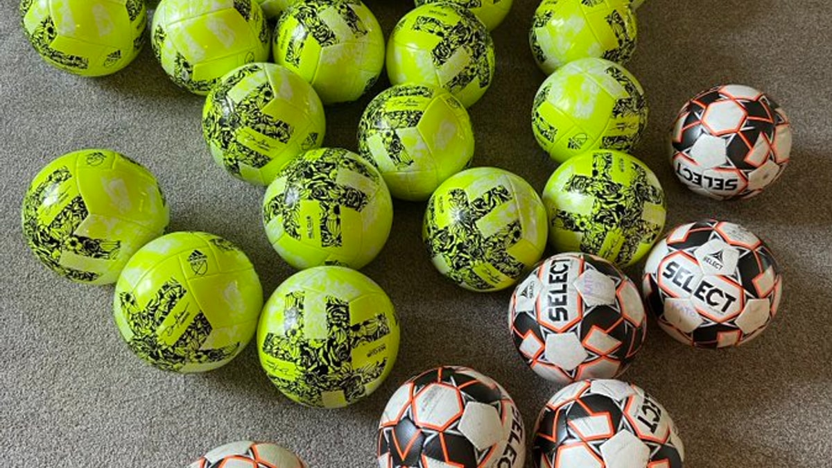 Soccer balls gathered on a sideline before a pressure check.